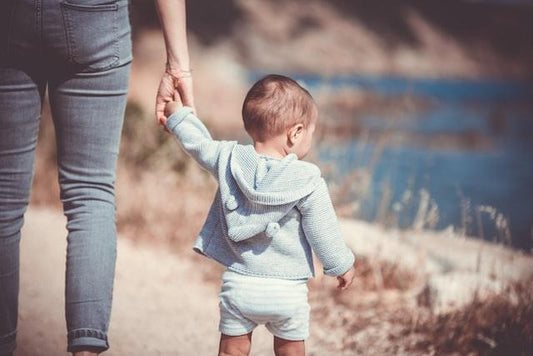 Baby holding a hand with an adult near a lake