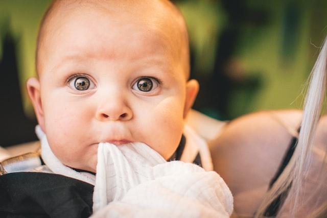 Baby holding a white cloth to their mouth while being held by an adult.