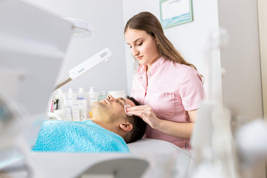 Skincare professional cleaning a man's face with a cotton pad during a facial treatment.