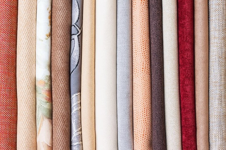 Assorted rolls of woven fabrics in different colors and textures.