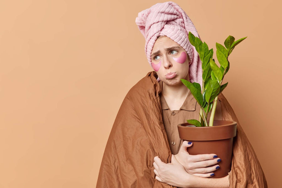 Woman with a towel wrapped around her hair holding a potted plant with a skeptical expression.